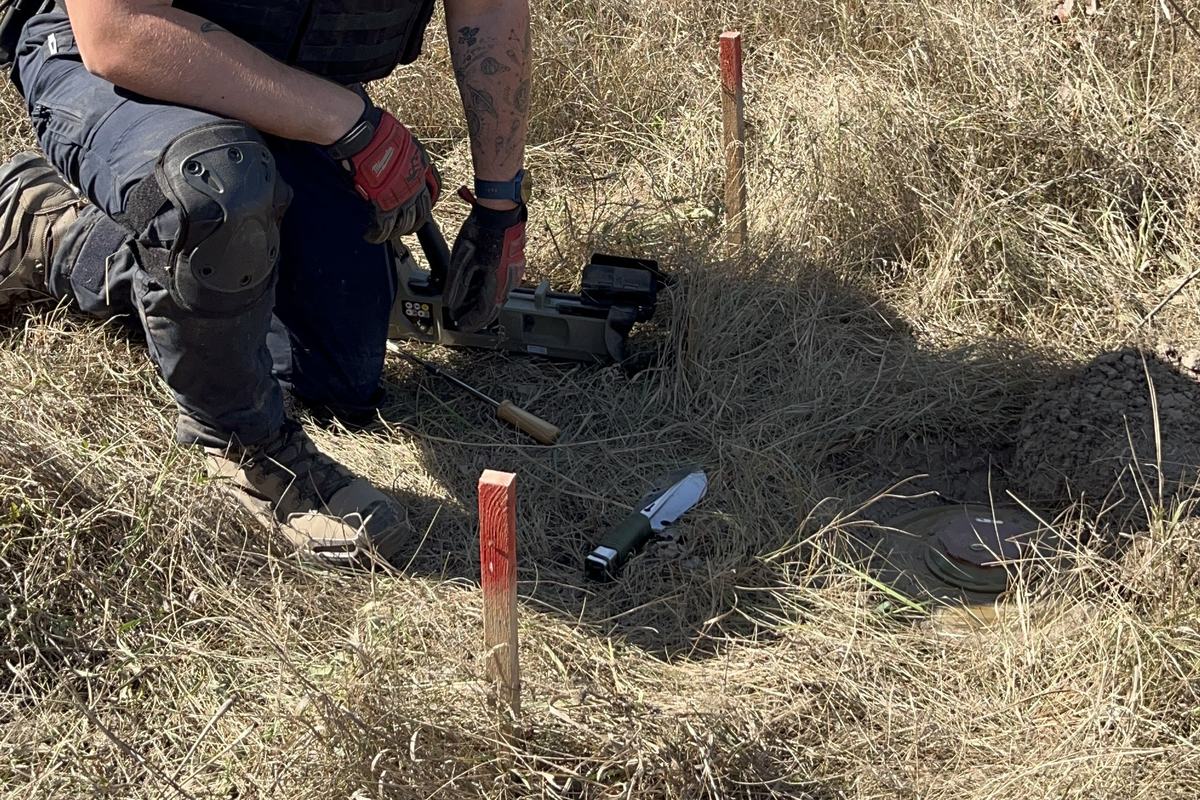 A deminer carefully excavating a marked, unexploded mine by hand